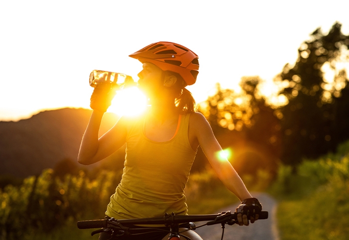 Woman on a bike drinking water at sunset